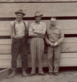 Bill Fallert, Charlie Ames, and Archie Simpson standing in front of stacked lumber